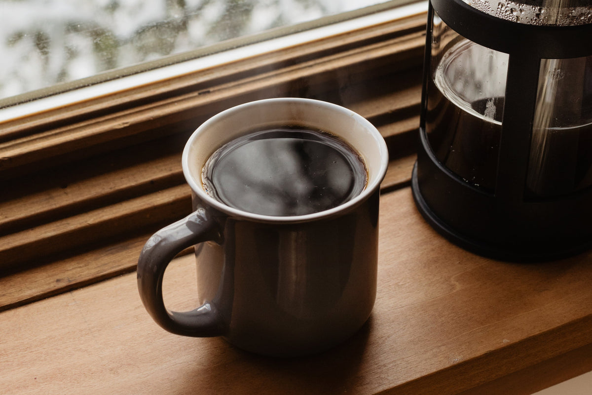 Kop kaffe og stempelkande i vindueskarmen med sne udenfor